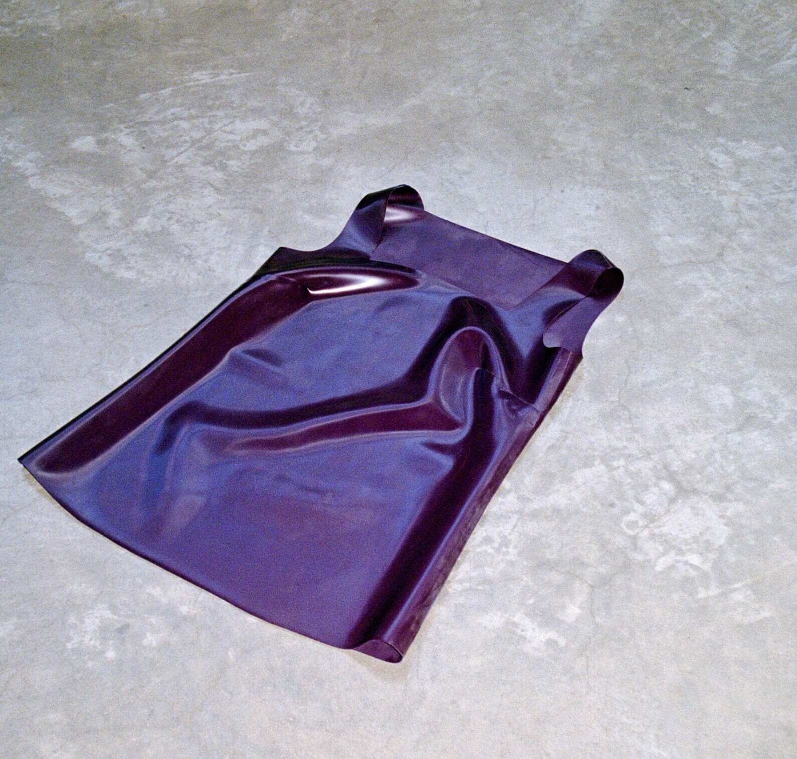 Luxury Handmade Latex Dress - Deep Purple Handmade deep purple latex dress with a sleek, minimalist design, displayed on a textured concrete floor. High-end latex fashion