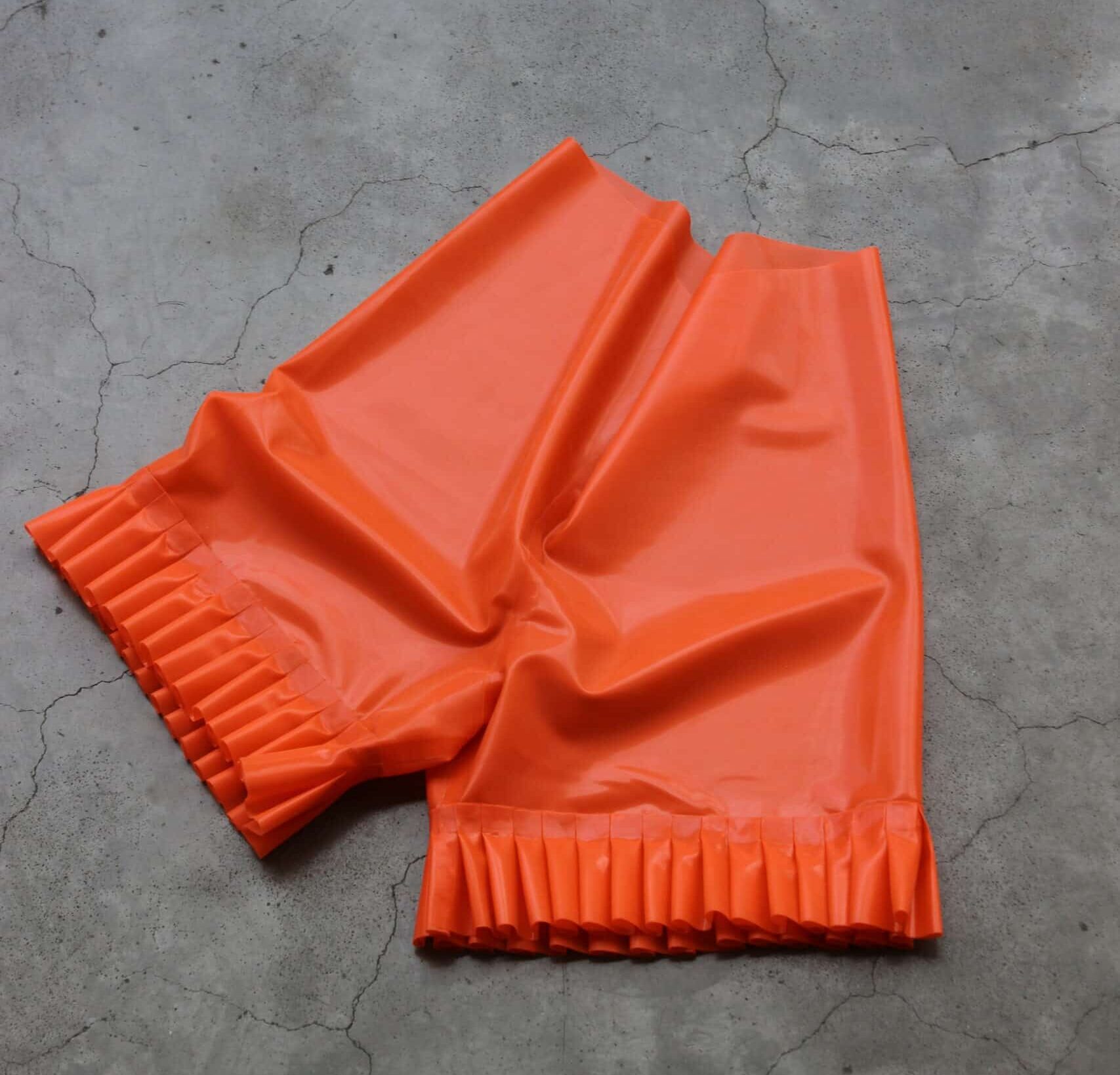 4-Le shorty à volants Latex ruffle shorts photographed flat on a raw concrete floor, showcasing the structured pleats at the hems and the smooth surface of the fabric.