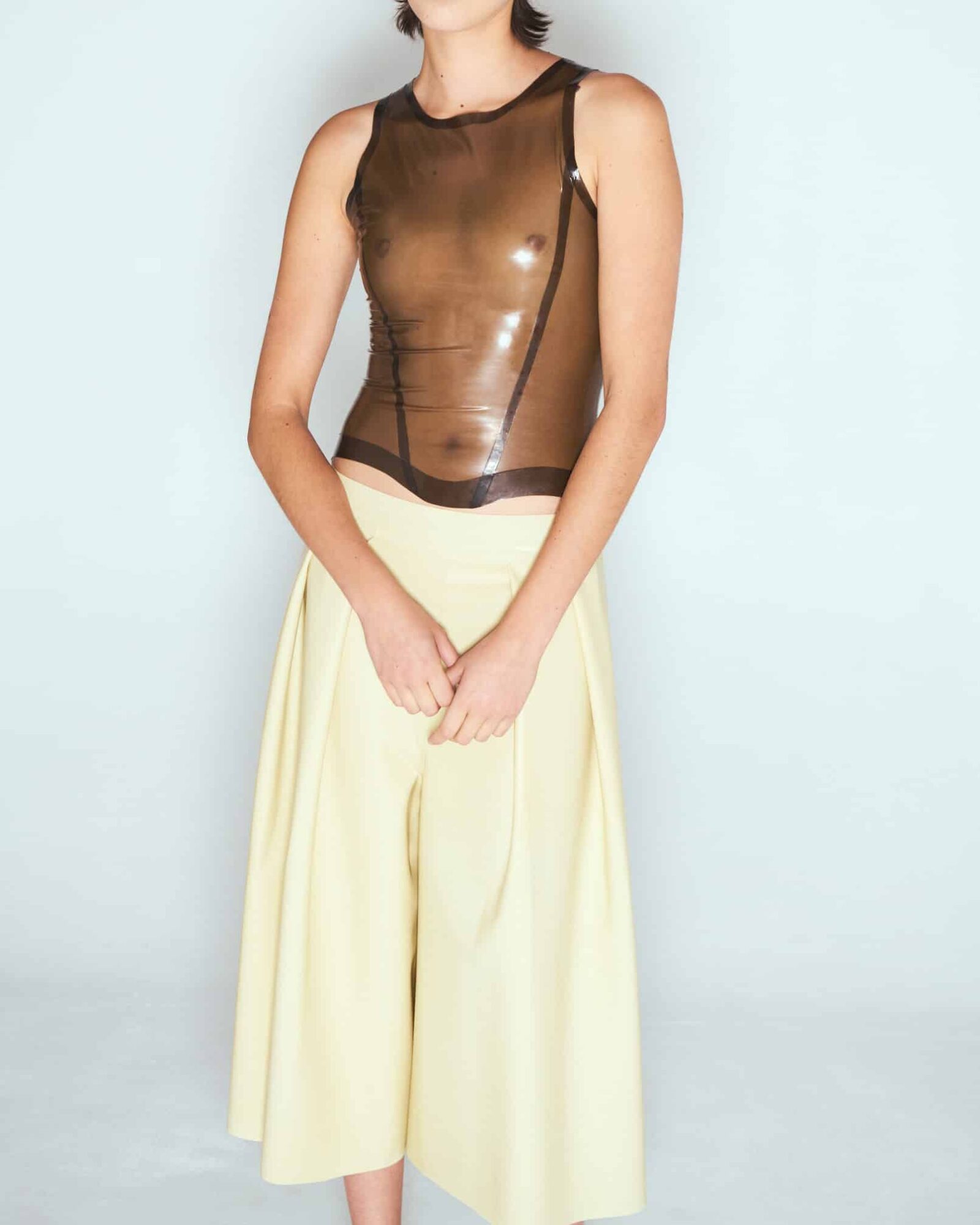 Model wearing a transparent smoky brown latex top and yellow culotte skirt by Sarah Chalal, handmade in Paris.